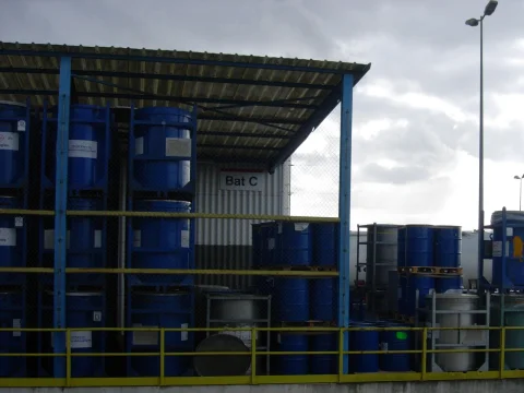 Blue chemical storage drums under a covered warehouse rack
